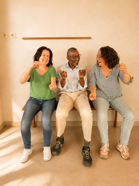 Trois participants assis sur un banc rient ensemble en réalisant un geste ludique